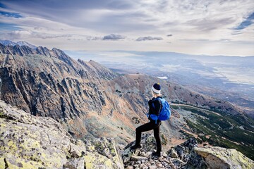 Obraz premium Beautiful blonde woman enjoys the moment while hiking in the Slovak Tatra Mountains on Mount Kryvan. She rests on the route and looks at the lake among the rocky peaks