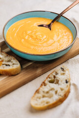 Creamy pumpkin soup garnished with  cooking sauce served in turquoise dish with slice of bread in rustic mood. Seasonal warm food. Autumn Appetiser 