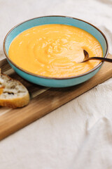 Creamy pumpkin soup garnished with  cooking sauce served in turquoise dish with slice of bread in rustic mood. Seasonal warm food. Autumn Appetiser 