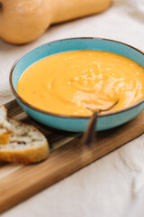 Creamy pumpkin soup garnished with  cooking sauce served in turquoise dish with slice of bread in rustic mood. Seasonal warm food. Autumn Appetiser 