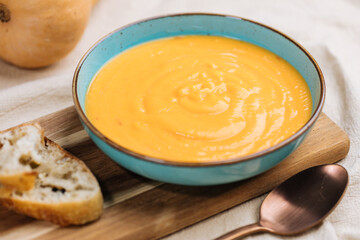 Creamy pumpkin soup garnished with  cooking sauce served in turquoise dish with slice of bread in rustic mood. Seasonal warm food. Autumn Appetiser 