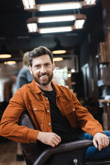 cheerful bearded man looking at camera while sitting in barbershop.