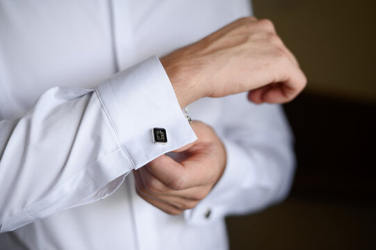 Portrait of a fashionable man fastening stylish cufflinks on the sleeves of his white shirt. Wedding day concept.