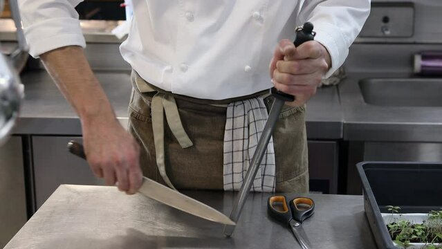 Chef sharpening a knife in a professional kitchen of a restaurant.