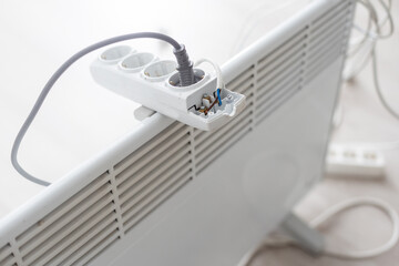 Electric heater plug inserted into extension cord. White radiator for home and office. House heating and comfort