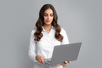 Portrait of a young happy business woman with a laptop over gray background.