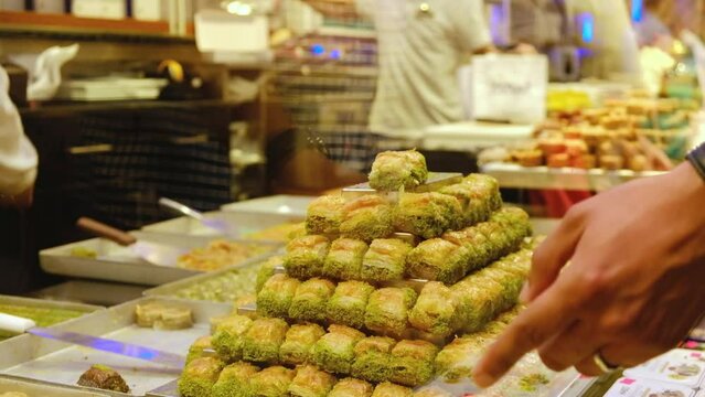 Stacks of baklava at foreground and hands of unrecognizable seller serves customers at traditional turkish delights shop. Showcase of turkish confectionery