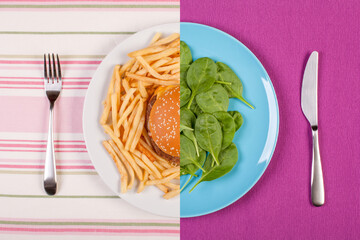 burger with french fries and fork on one side of the dividing line and baby spinach leaves and knife on another half. flat lay diet concept image of healthy and unhealthy eating