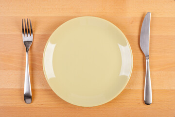 flat lay image of empty green plate, fork and knife on wooden table