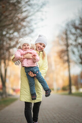 Portrait of a young beautiful mother with her daughter on the autumn street.