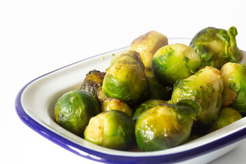 Brussels sprouts, oven roasted in olive oil,  in an enamel dish bowl. Isolated on a white background
