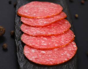 Smoked sausage slices on a black stand under dark lighting. Shallow depth of field
