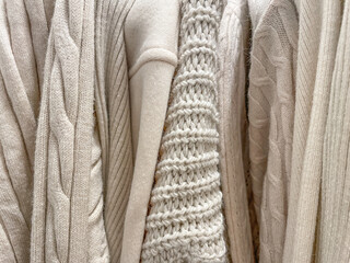 Texture background photo of different knitted sweaters and jumpers of beige cream color hanging in stack in the store.