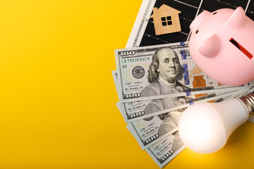 Flat lay composition with solar panel, LED lamp, piggy bank, house model and money on yellow background. Money saving and clean energy concept. Ecology and sustainable development concept. 