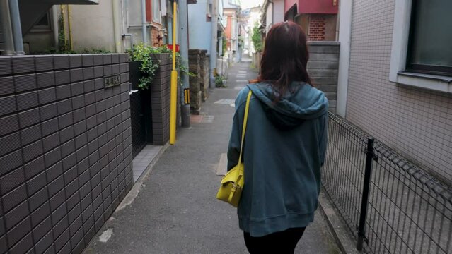 Japanese woman walks through a tiny street. Back shot. No face.