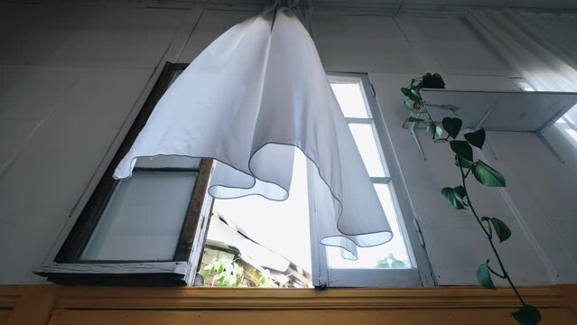 White long curtains flying from the wind hanging on an open window on summer day