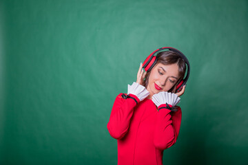 pretty cheerful girl listening different song rock dancing isolated on green color background.Positive smiling young woman with red headphones in red dress while listening music. She enjoying song