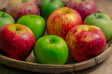 red and green apples isolated in wicker basket with wooden background