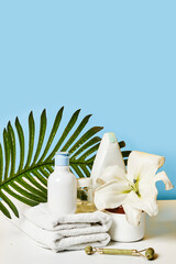 some flowers and towels on a white table with a blue wall in the background behind it is a bottle of lotion