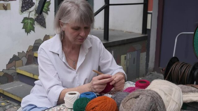 Happy elderly woman sitting in the garden with crochet threads and needlework