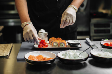 Closeup of chef hands in gloves preparing sushi rolls.