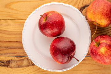 Several red juicy apples with a white plate on a wooden table, macro, top view.