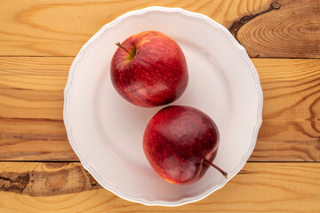 Two red juicy apples with a white plate on a wooden table, macro, top view.