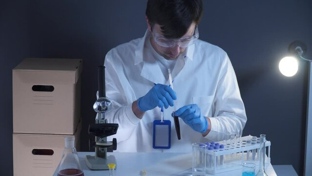 Scientist working with blood sample in laboratory. Lab analyst analyzes a blood slide. Doctor or pathologist drops a humans red blood on glass plate. Biological material to identify the virus. 