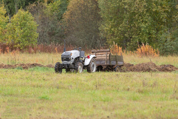 A tractor with a trailer stands on a field with grass and plowed land
