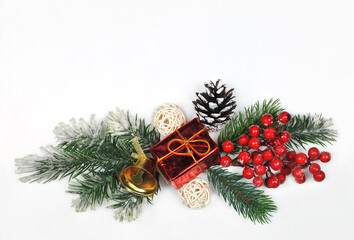 A border from snowy pine tree branches, decorative viburnum berries ,cone ,golden bell, gift and  rattan snowballs on white background. Christmas greeting concept. Free space for message