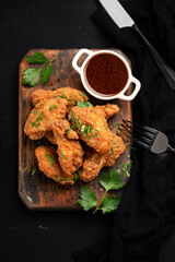 A large portion of breaded fried chicken wings with a golden crust, parsley and barbecue sauce. Grilled chicken pieces served on a wooden board