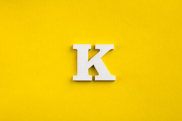 Obraz premium Alphabet letter K - White wood letter on yellow colored background
