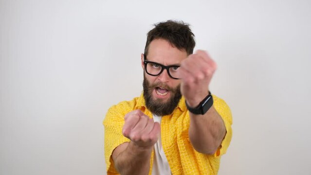 Funny bearded hipster guy in glasses looking like a nerd imitates karate and boxing punches while looking at the camera.