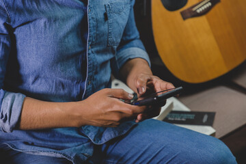 joven sentado en su sala, leyendo un libro, estudiando, guitarra y celular. concepto de estudiante o impartiendo y ense&ntilde;ando lectura