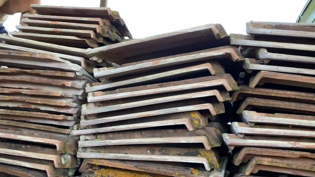 Stack of demolished red clay roof tiles outdoor, weathered ceramic shingle unusable for covering house roof, construction site garbage ready for recycle. Dismantling ruined terracotta roof tiles