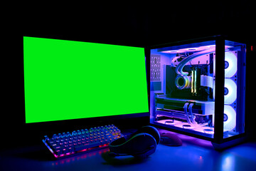 Gaming PC with RGB LED light, keyboard, mouse, headphones and monitor with green screen, copy space. Gamer's workspace. Modern powerful liquid-cooled Computer in a glass case