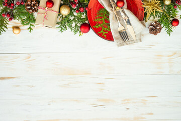 Christmas table setting with red plate, cutlery and christmas decorations on white wooden...