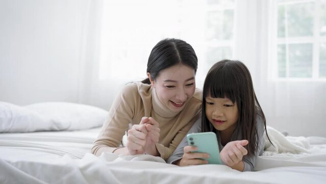 Young happy woman with cute little daughter taking photo selfie with mobile phone, enjoying technology network together at home bedroom, happy family mothers day, education technology concept.