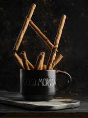 Cinnamon sticks in a coffee black cup on a black background. Stylish culinary composition. Fragrant spices and seasonings, ingredient for confectionery, hot drinks.