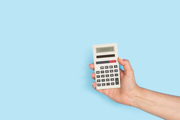 Mano de mujer sosteniendo una calculadora sobre un fondo celeste liso y aislado. Vista de frente y...