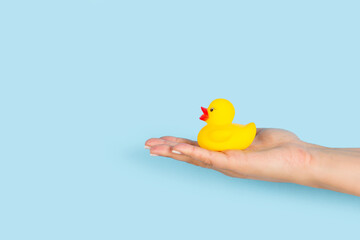 Mano de mujer sosteniendo un pato de goma amarillo sobre un fondo celeste pastel liso y aislado. Vista de frente y de cerca. Copy space