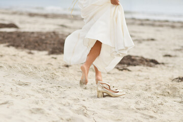 Bride in white dress and golden shoes on the beach