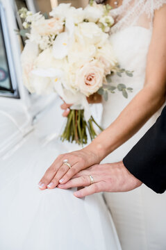 Bride and Groom showing off wedding rings on a white vintage luxury car, bridal bouquet in background, color vertical image
