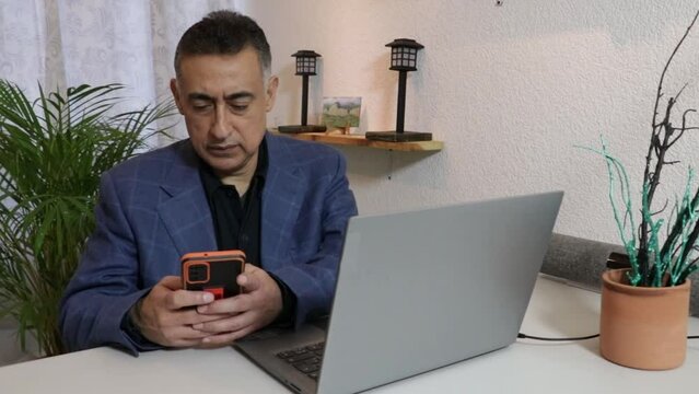 Hombre ejecutivo latino usando celular frente a computadora