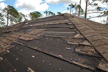 Wind damaged house roof with missing asphalt shingles after hurricane Ian in Florida. Repair of home rooftop concept