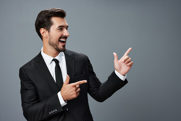 Business man has his hands up pointing his finger and smiling with his teeth open mouth in a business suit on a gray background portrait