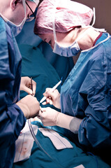 Surgeon and his assistant performing cosmetic surgery in hospital operating room. Surgeon in mask wearing loupes during medical procadure. Breast augmentation, enlargement, enhancement, breast cancer