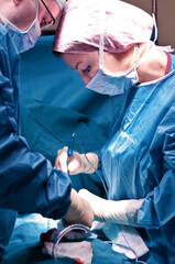 Surgeon and his assistant performing cosmetic surgery in hospital operating room. Surgeon in mask wearing loupes during medical procadure. Breast augmentation, enlargement, enhancement, breast cancer