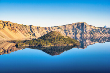 View of Wizard Island in Crater Lake with mirror-like reflections on a calm and clear summer morning.