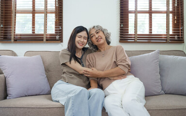 Portrait loving adult asian people daughter and senior mature mom hugging on couch.